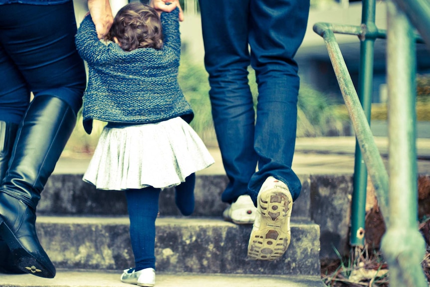 Two parents hold the hands of a toddler.