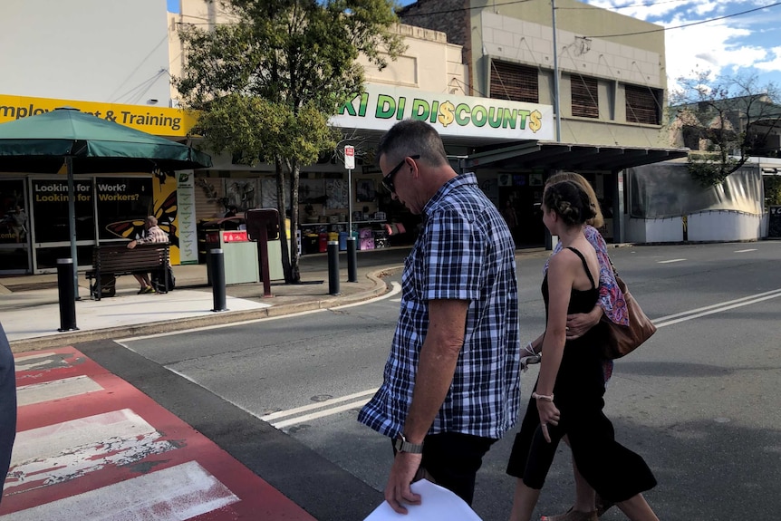 A man with sunglasses and a checked shirt crosses a road with a woman and a girl.