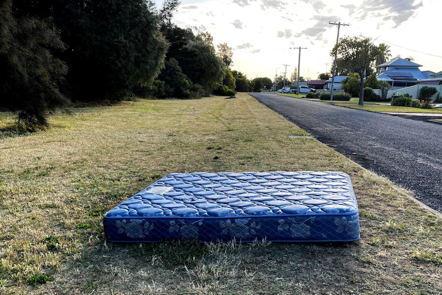 A single blue mattress on a a suburban sidewalk.