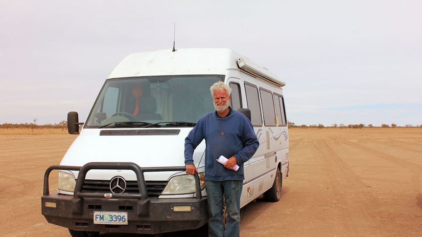 Ian Blair standing on red sand, next to his white motorhome.