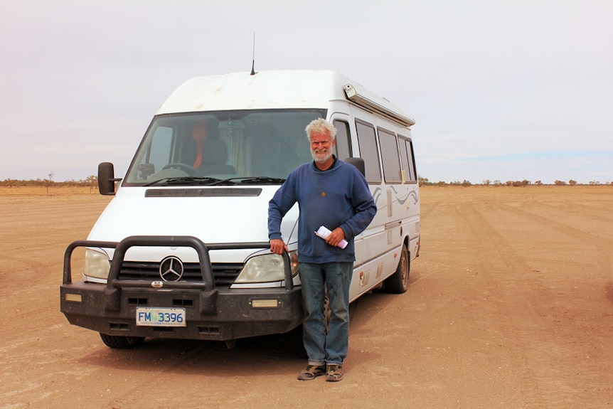 Ian Blair standing on red sand, next to his white motorhome.