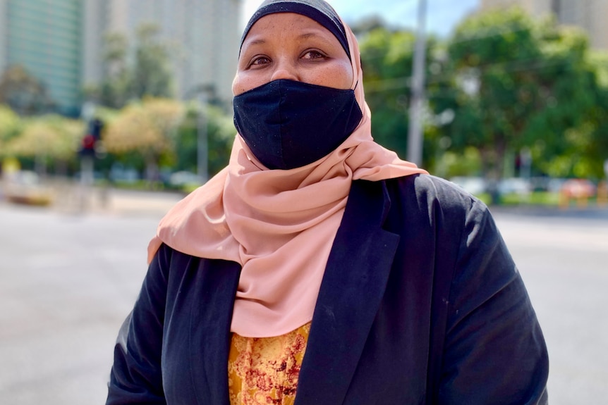 A woman wearing a mask standing behind public housing towers.