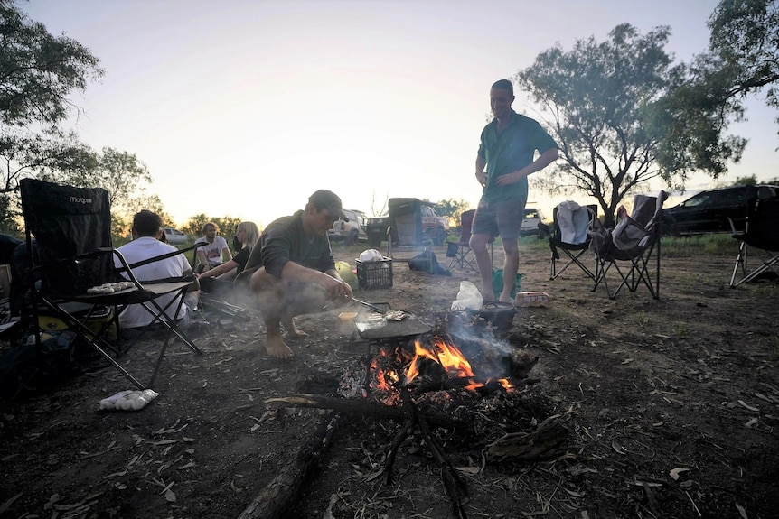 Young man lighting a fire with a circle of friends.