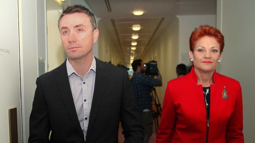 James Ashby stares blankly ahead as he walks with Pauline Hanson, whose lips are pursed as she looks directly at the camera.