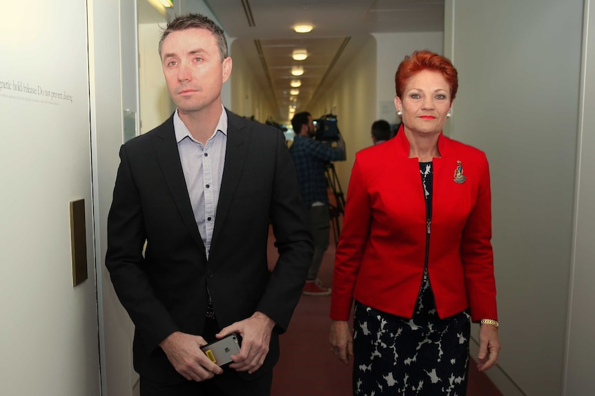 James Ashby stares blankly ahead as he walks with Pauline Hanson, whose lips are pursed as she looks directly at the camera.