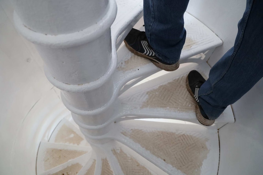 A person wearing a pair of black sneakers and jeans walks up spiral staircase halfway through being painted white