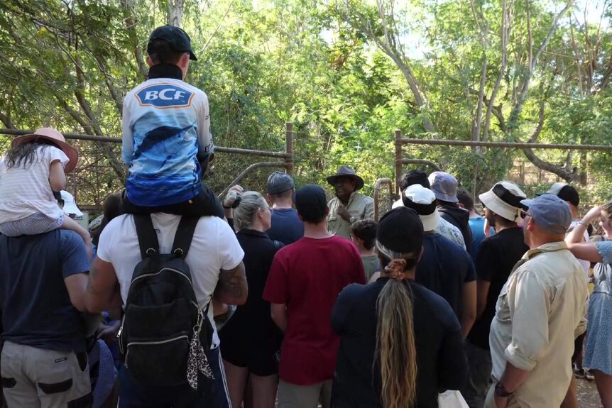A group of adults and children standing together, watching a tour guide at a crocodile park.