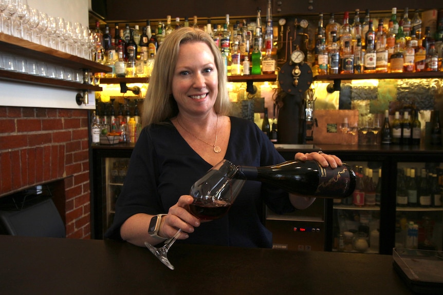 A woman in a bar, pouring a wine.