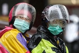 Two motorcyclists in multi-coloured rain jackets wearing helmet and masks in rainy weather