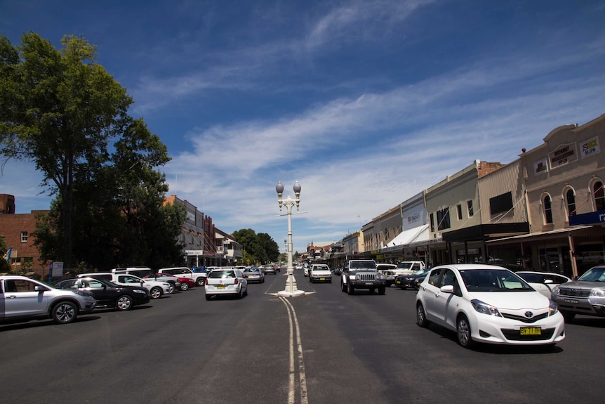 A country city street with cars, old fashioned lamp post and shop fronts