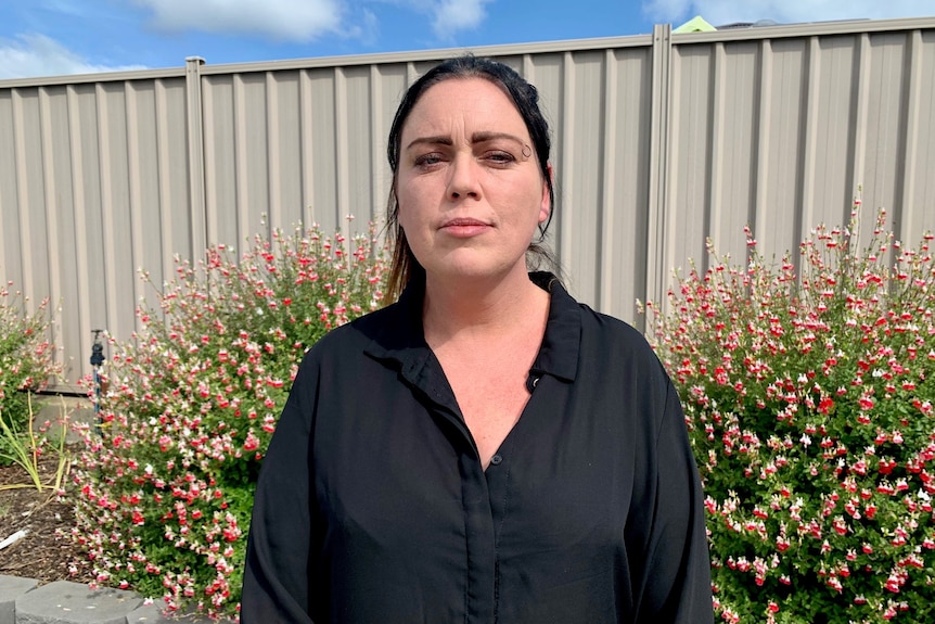 A woman standing on front of a fence looks seriously at the camera.