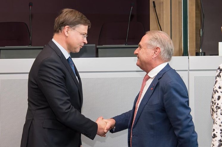 Two men, wearing dark suits, shake hands.