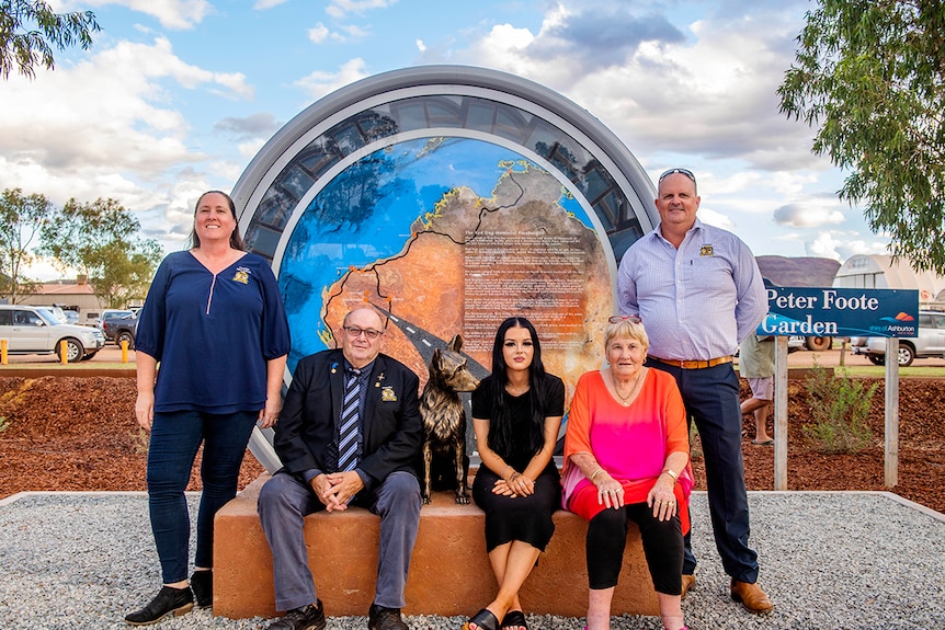 Three people sit alongside a bronze puppy statue while two people stand next to them