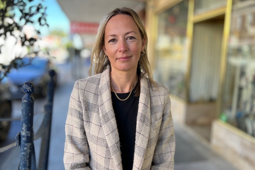 Anneke Thompson poses for the camera, an out-of-focus row of shops behind her, wearing a check jacket.