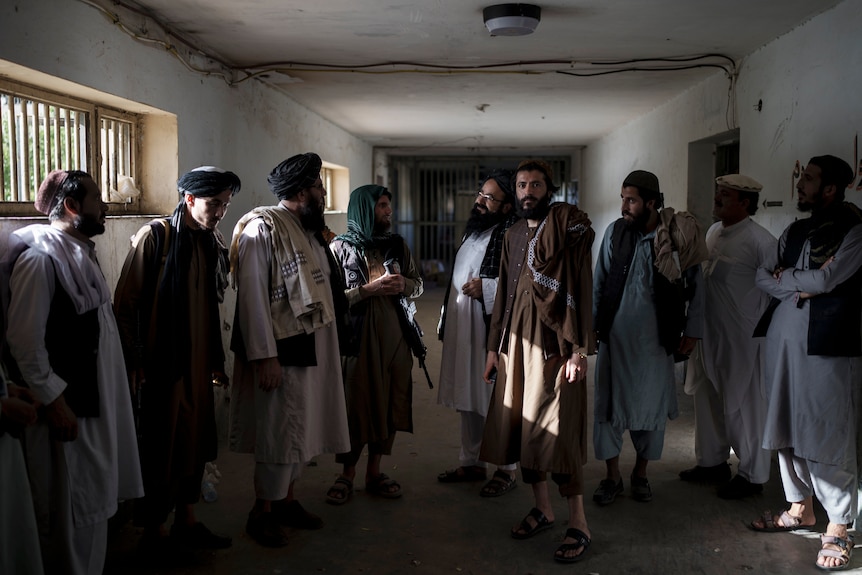 Nine men stand in a concrete corridor as light streams in through prison bars. 