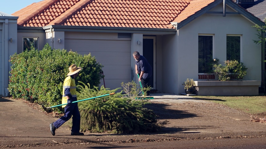 Two men with brooms outside a home cleaning up mud after heavy rain.