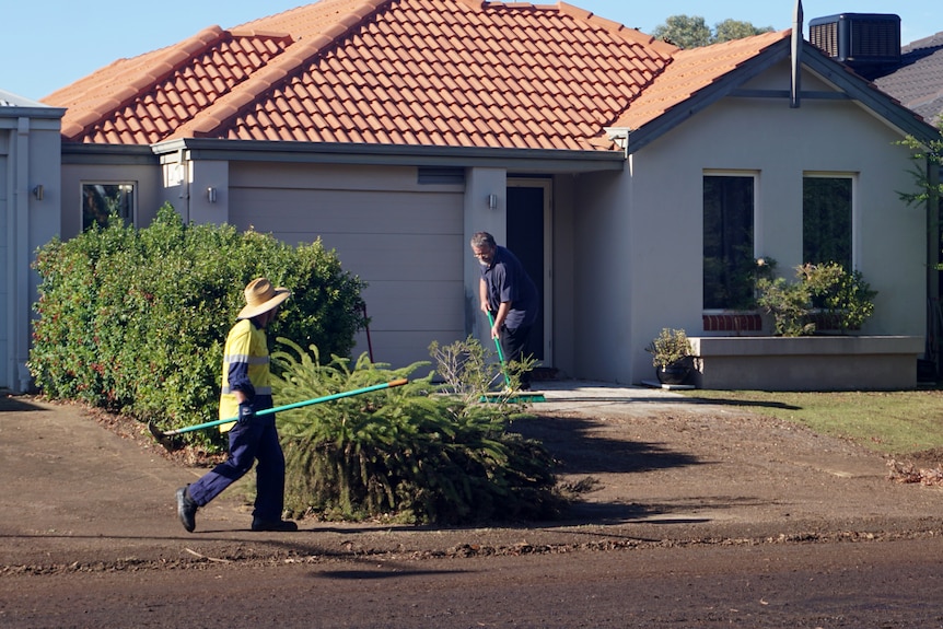 Two men with brooms outside a home cleaning up mud after heavy rain.