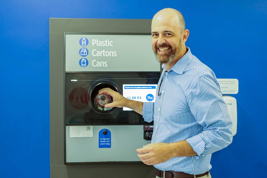 Man holding a bottle in a refund machine kiosk.