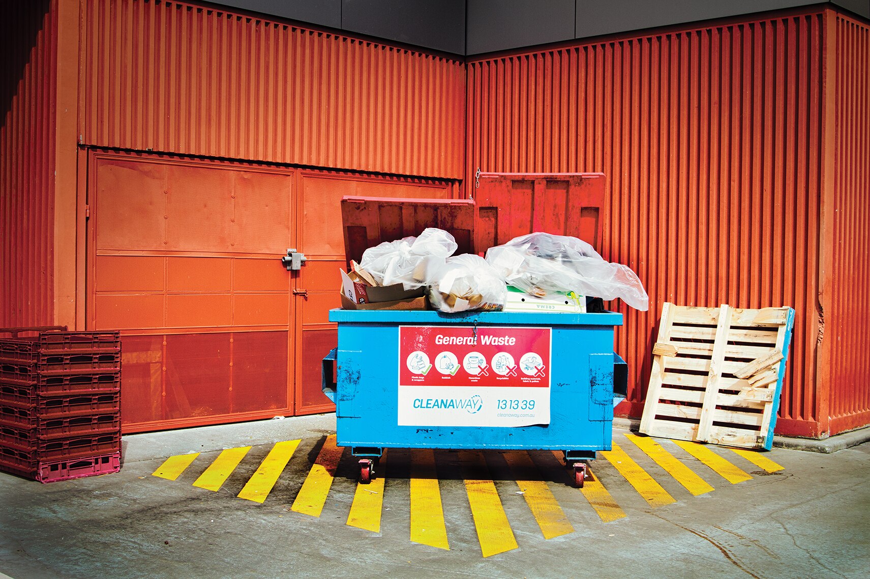 a dumpster full of rubbish sits in front of a red wall