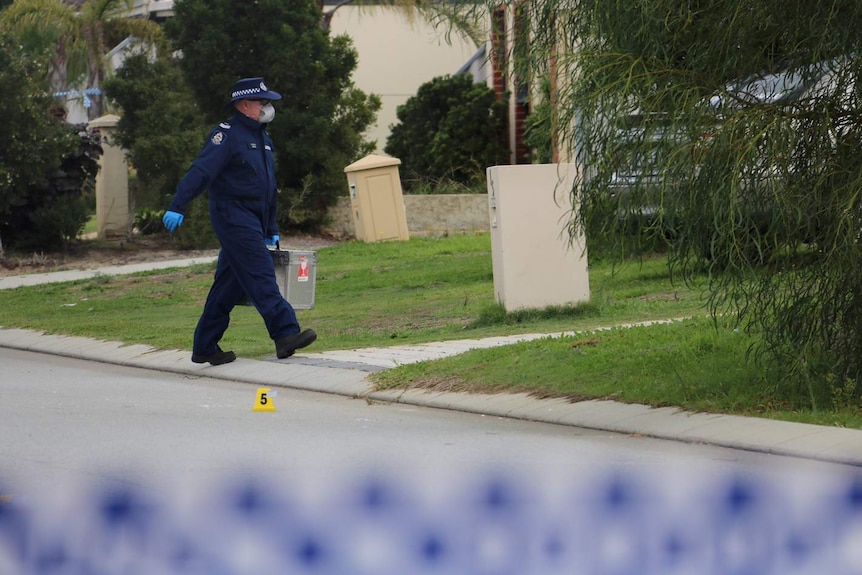 A forensics officer in a blue jumpsuit walks carrying a large silver briefcase on Cassia Link in Banksia Grove.