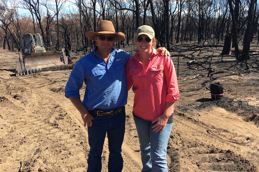 Matt Cherry, left, stands next to Shelley Piper in front of burned trees. They have their arms around each other.