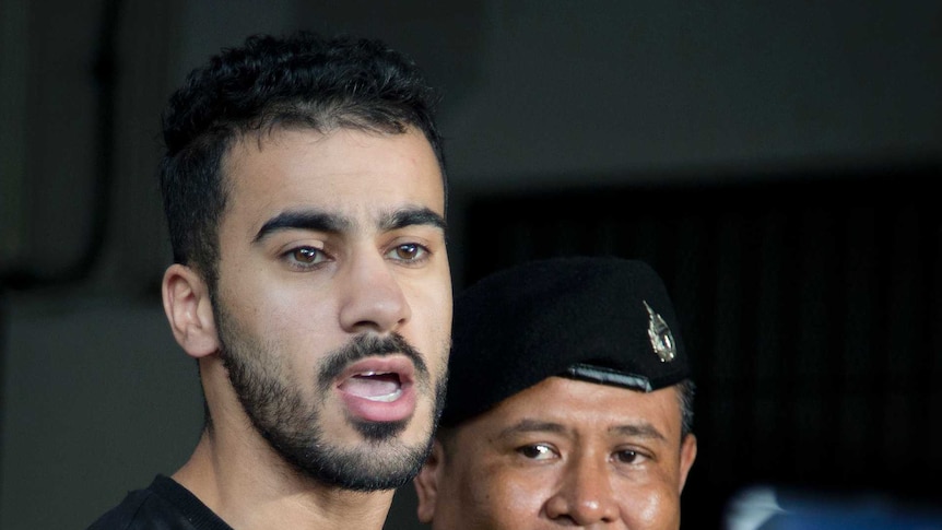 Bahraini football player Hakeem AlAraibi enters court as two policemen stand next to him