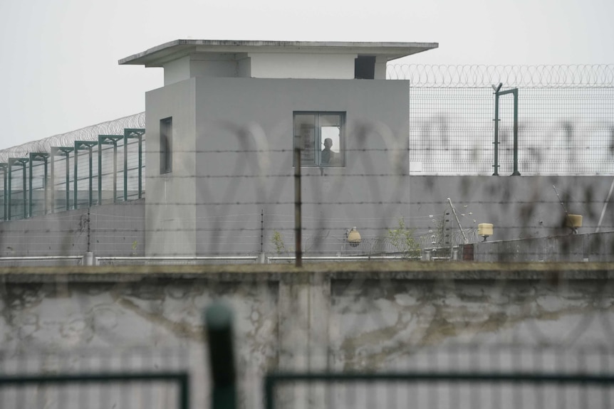 A man is seen in a guard tower building of Qingpu Prison, surrounded by high fences and barbed wire.