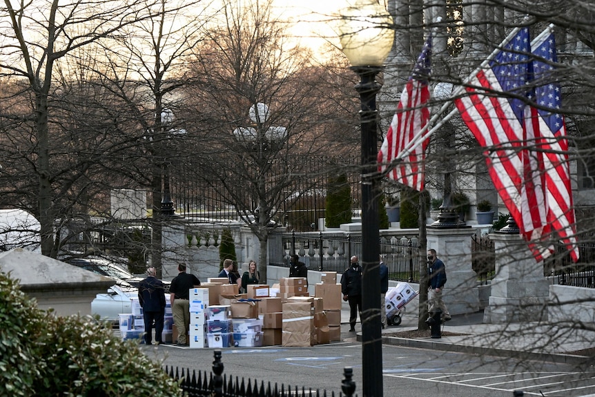 A big pile of cardboard boxes on a street corner with a row of US flags hanging from street poles 