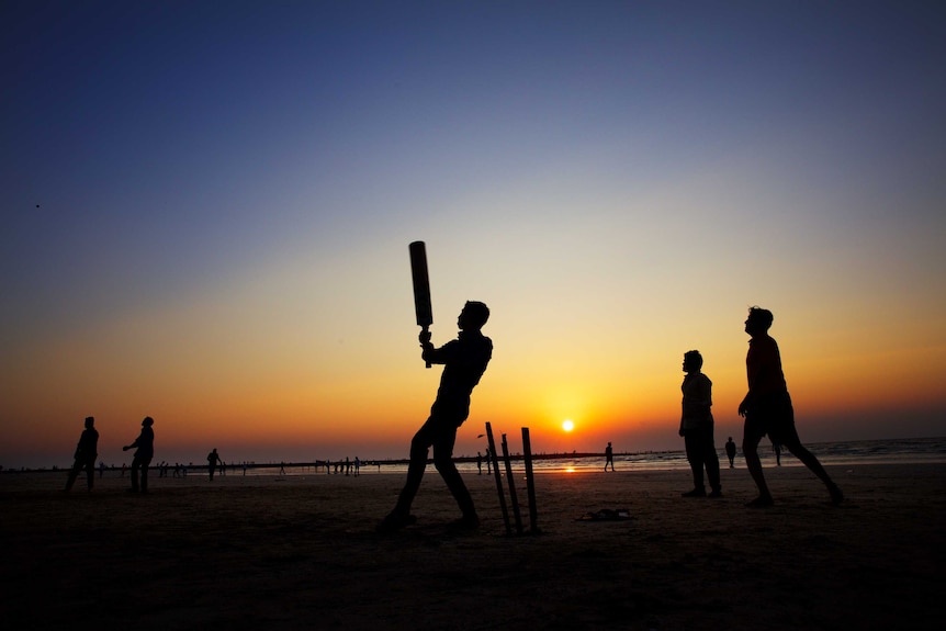 People playing cricket against sun backdrop.