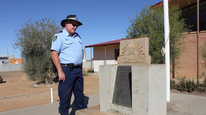 A police officer looks at a war memorial plaque.