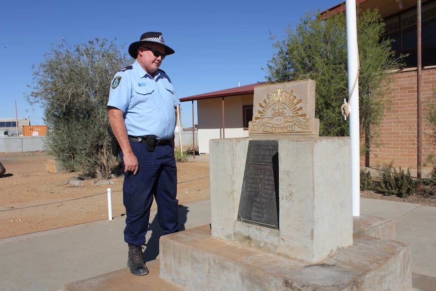 A police officer looks at a war memorial plaque.