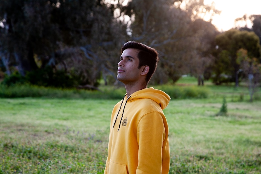 A young man in a yellow jumper looks up at the sky