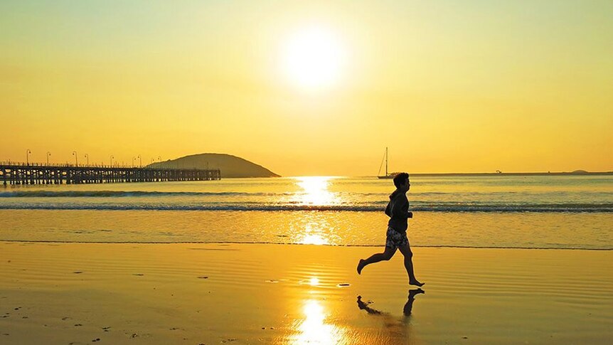 A man running on a beach at sunrise.