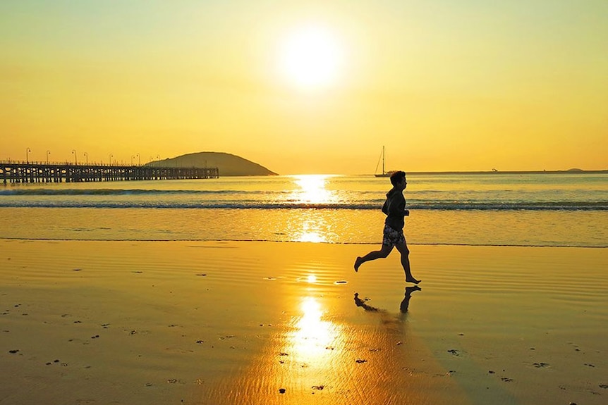 A man running on a beach at sunrise.