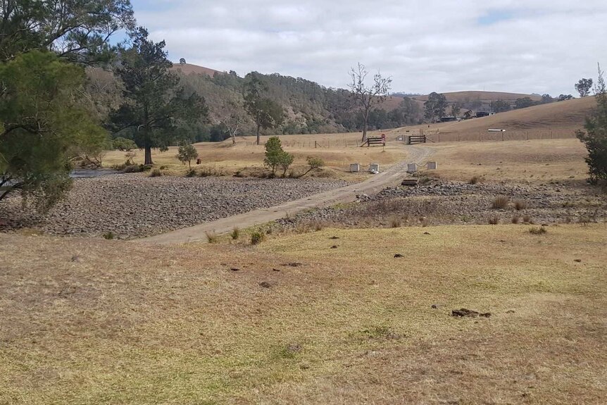 Brown farmland, with a dry river crossing and road running through it.