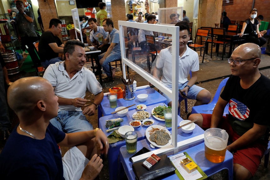 People sit at a table with a plastic partition attached as a protective measure against the spread of COVID-19.