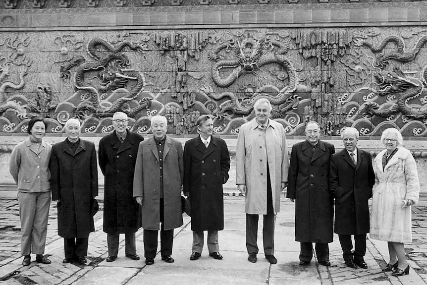 一些中年男女站在北京天坛九龙壁前合影。
