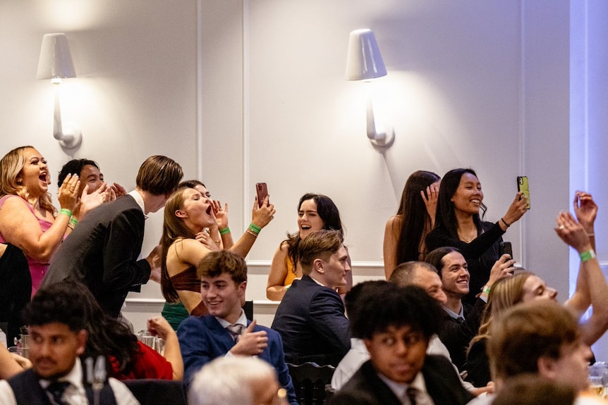 Young people stand cheering and taking photos