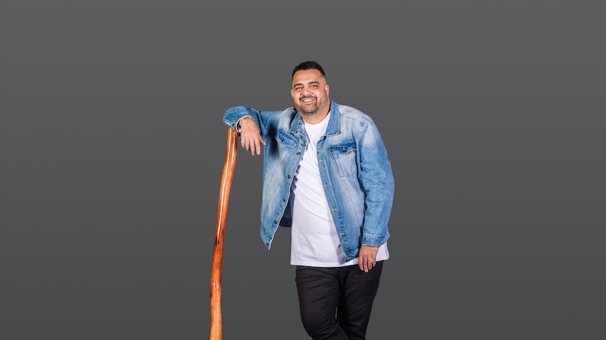 a tall indigenous man standing up with a didgeridoo