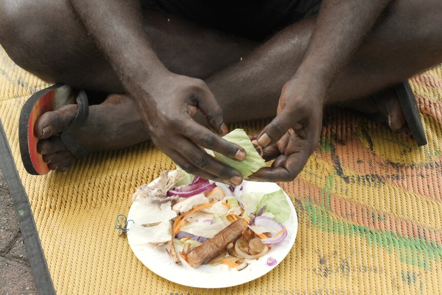 A man's hands picking up lettuce from a paper plate on the ground