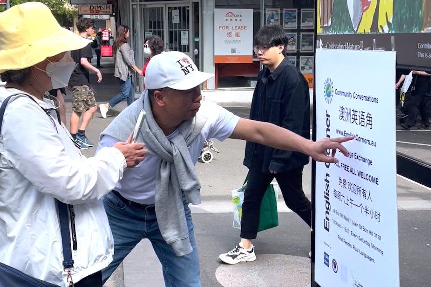 A man pointing at a poster and talking to a woman standing beside him