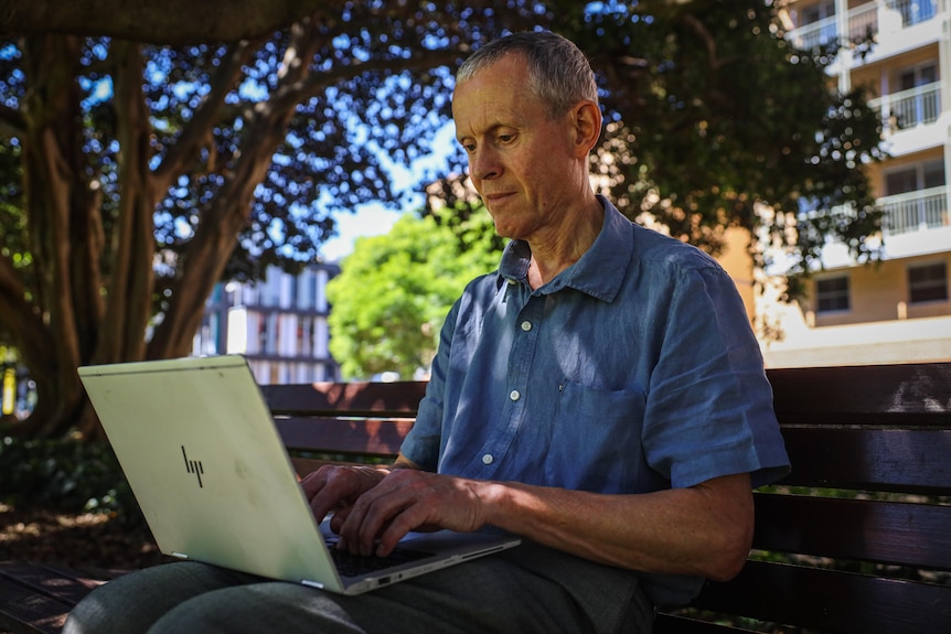 Professor Hal Pawson sitting on  park bench using his laptop.