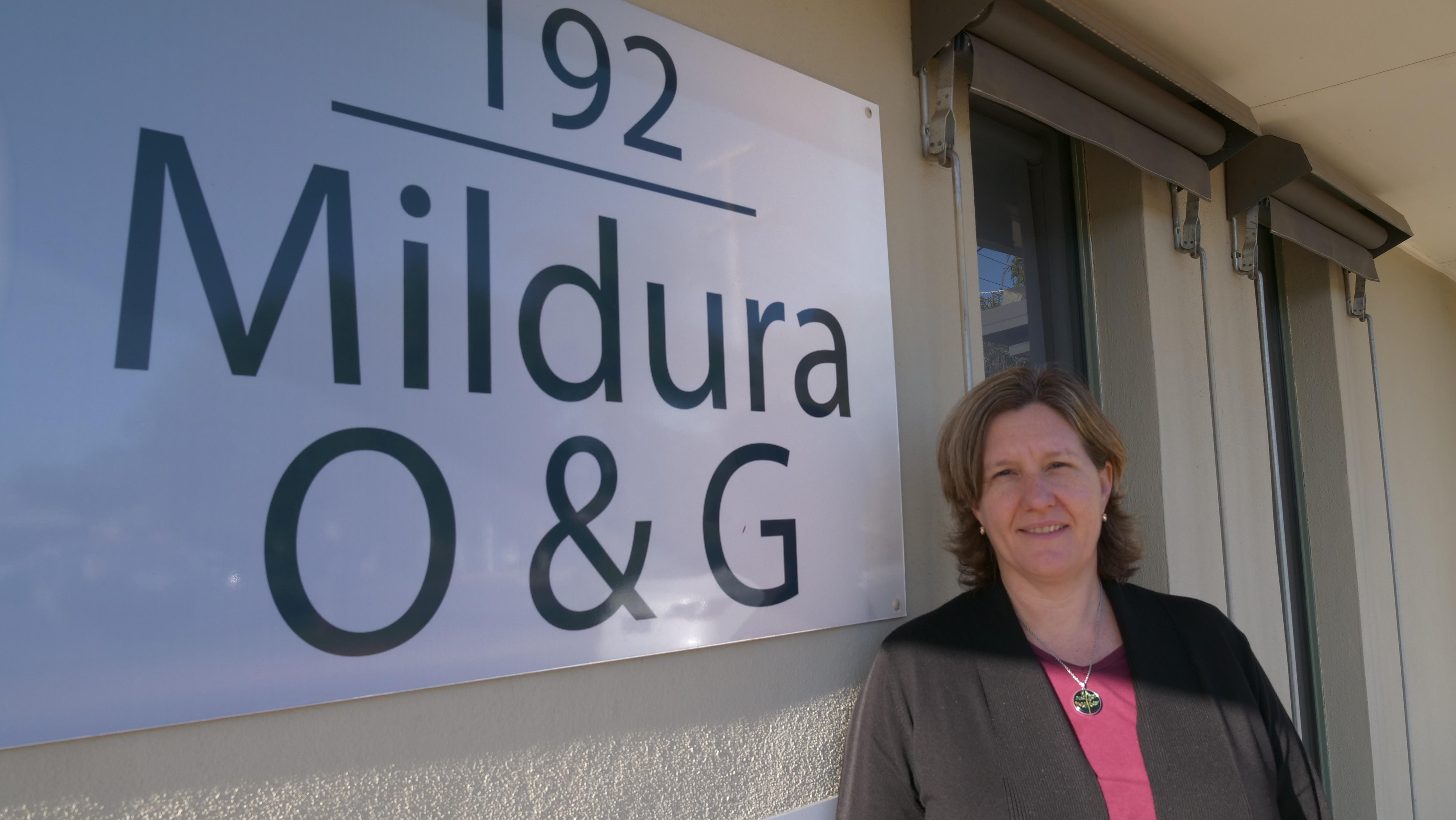 Brunette woman with shoulder-length hair smiling next to "Mildura O&G" sign