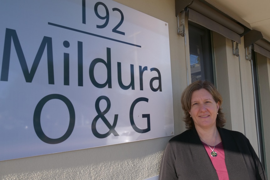 Brunette woman with shoulder-length hair smiling next to "Mildura O&G" sign