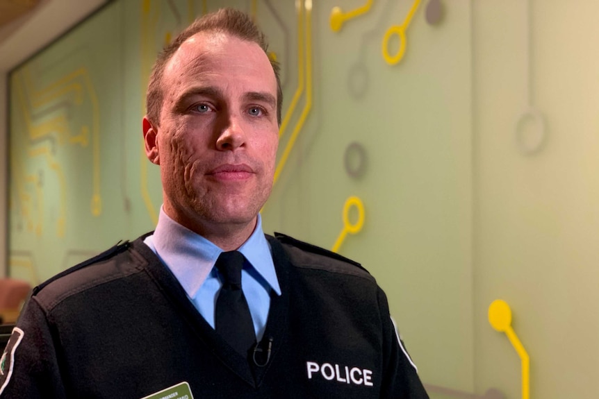 A man in Australian Federal Police uniform sits in front of a wall with a motherboard print.