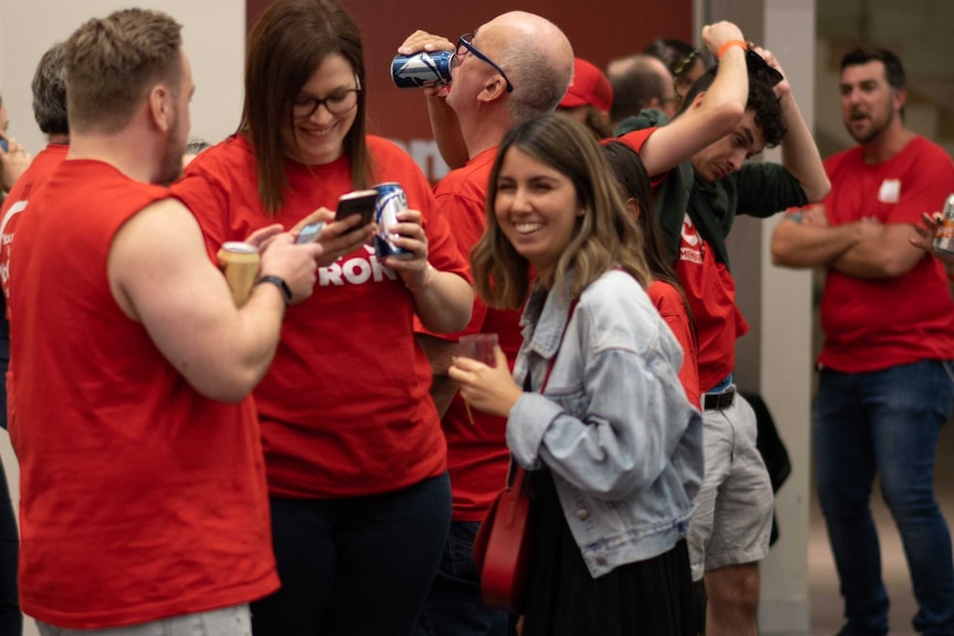 Labor supporters in red shirts smiling and drinking.