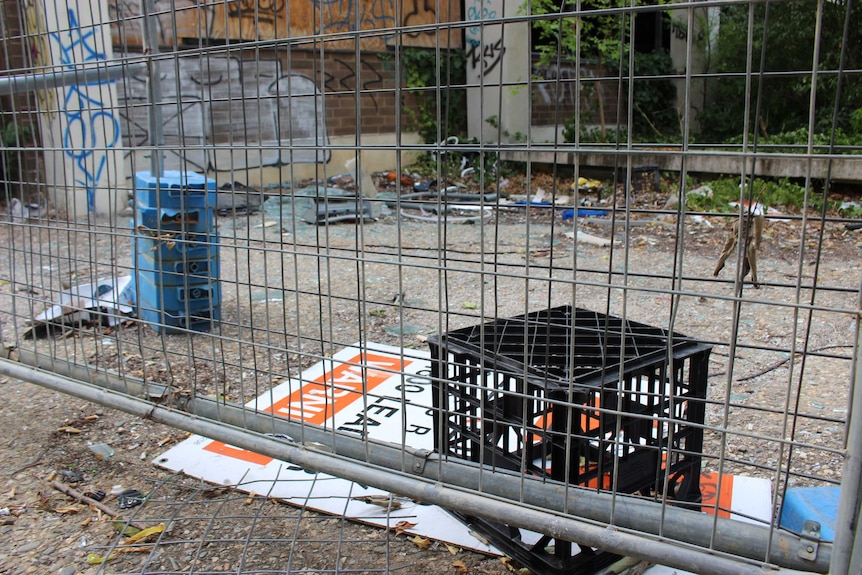 A crate and other rubbish behind a fence surrounding an abandoned building.