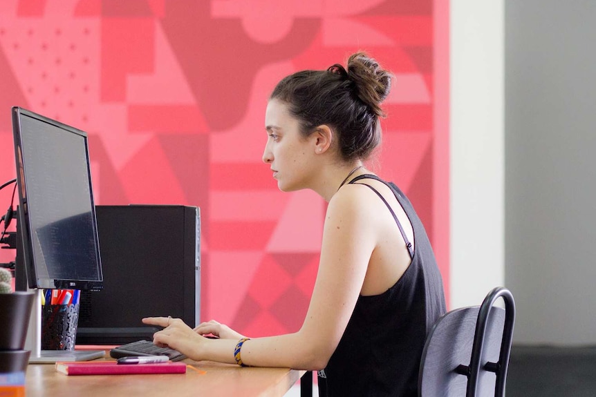 Young woman looking exasperated at a PC against a bright background in an office