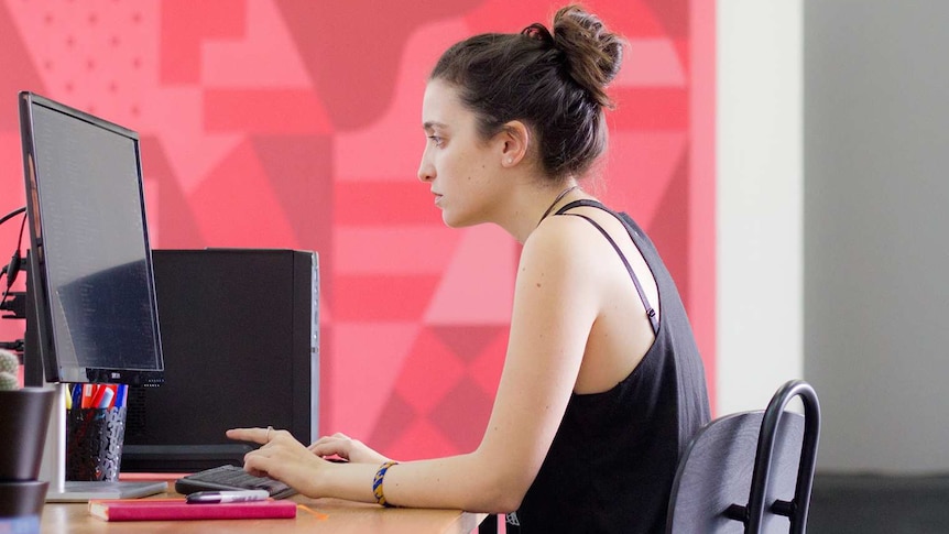 Young woman looking exasperated at a PC against a bright background in an office to depict the reality of online moderating.