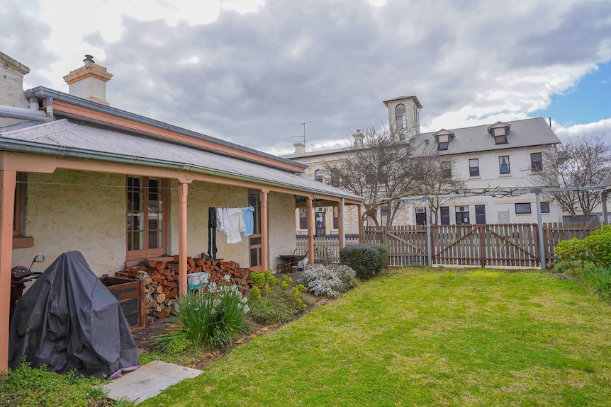 An white picket fence and flower pots line an old stone home with French windows and a wrap-around verandah.